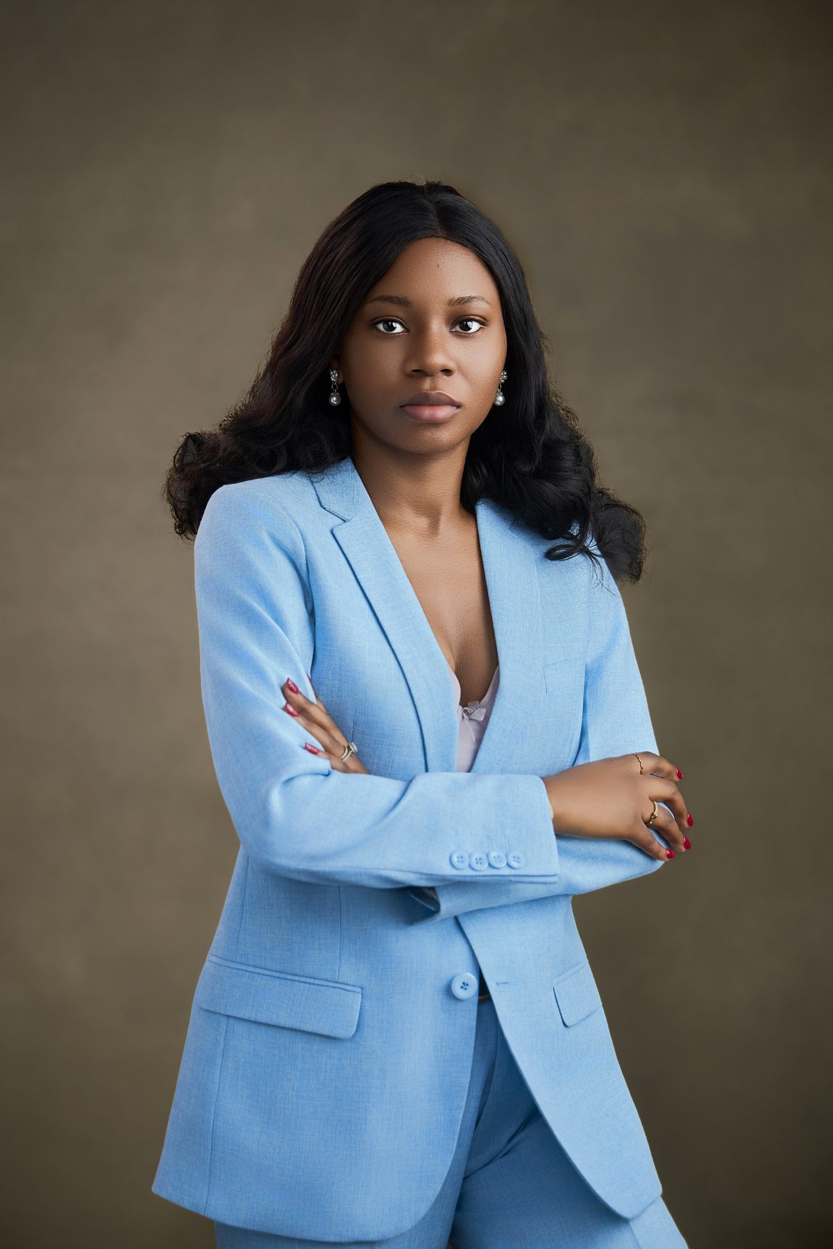 Portrait in a tailored sky-blue suit against a warm olive backdrop.