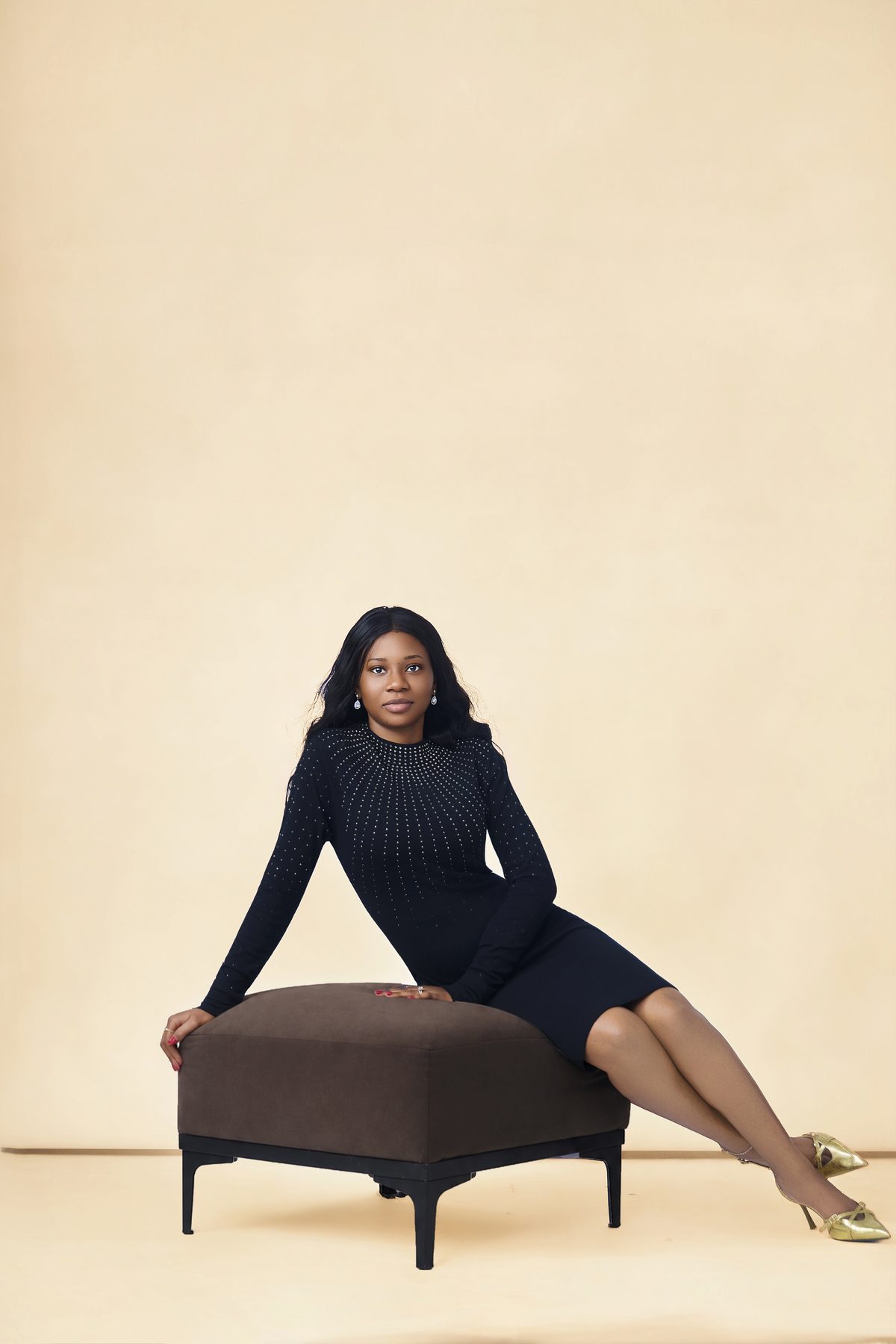 Editorial studio portrait in a black knit dress against a soft cream backdrop.
