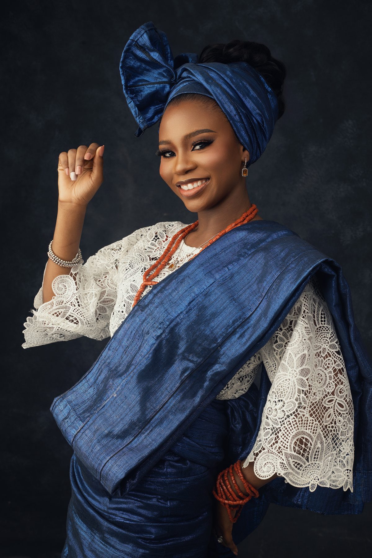 Portrait in a blue aso-oke gele and lace blouse with coral beads.